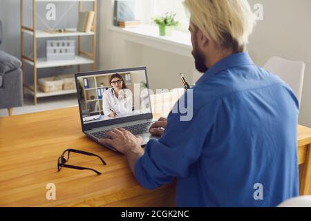 Un giovane è a casa e chiama un medico online utilizzando un computer portatile. Una dottoressa sullo schermo di un computer portatile fa una consultazione medica su Internet. Foto Stock
