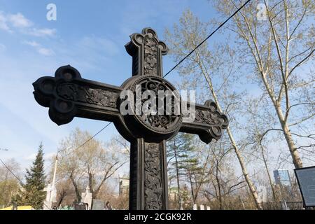 Antica croce forgiata in ferro nero costeggiata tra il cielo nel cimitero di Troitskoye (1842) della città di Krasnoyarsk, in primavera. Foto Stock