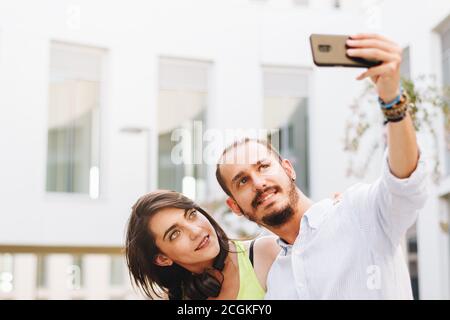 Giovane coppia che fa un selfie seduto su una panchina al campus. Foto Stock