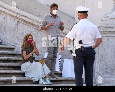 Turismo a Roma: L'ufficiale della polizia della Città armata informa la giovane coppia turistica che sedersi sulla famosa Piazza di Spagna è vietato dalla legge locale Foto Stock