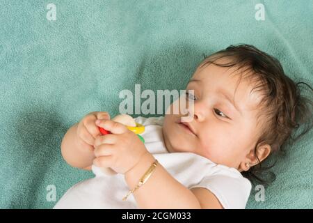 bambina di 6 mesi sulla schiena ravvicinato tenendo ed esaminare il sonaglino del giocattolo che sta tenendo con entrambe le mani Foto Stock