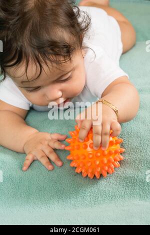 bambina di 6 mesi sullo stomaco vicino tenere ed esplorare la sfera di plastica sconnessa tenerla e toccarla con mano e dita Foto Stock