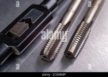 Utensili per il taglio di filettature metalliche. Accessori in acciaio per fabbri. Sfondo chiaro. Foto Stock