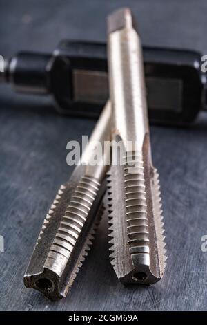 Utensili per il taglio di filettature metalliche. Accessori in acciaio per fabbri. Sfondo chiaro. Foto Stock