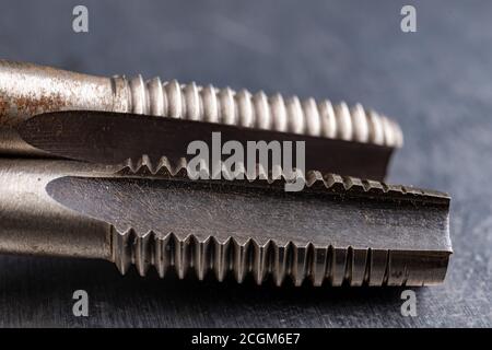 Utensili per il taglio di filettature metalliche. Accessori in acciaio per fabbri. Sfondo chiaro. Foto Stock