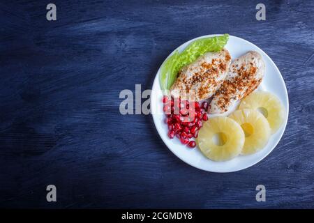 Filetti di pollo fritti con lattuga, ananas e semi di melograno su sfondo di legno nero, spazio copia, vista dall'alto. Foto Stock
