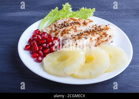 Filetti di pollo fritti con lattuga, ananas e semi di melograno su fondo di legno nero, spazio copia, primo piano. Foto Stock