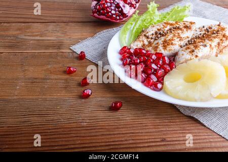 Filetti di pollo fritti con lattuga, ananas e semi di melograno su fondo di legno marrone, spazio copia, primo piano. Foto Stock