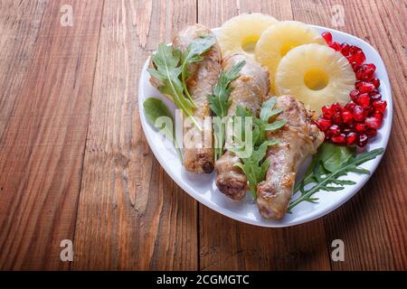 Cosce di pollo fritte con rucola, ananas e semi di melograno su sfondo di legno marrone, spazio copia, primo piano. Foto Stock