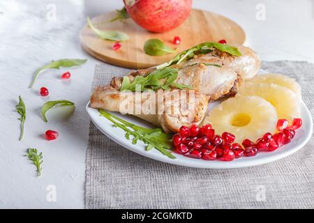 Cosce di pollo fritte con rucola, ananas e semi di melograno su sfondo bianco di legno, spazio copia, primo piano Foto Stock