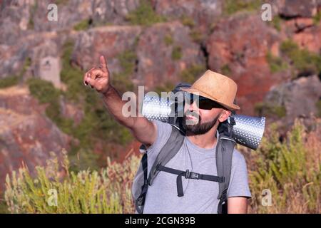 Uomo ispanico trekking con occhiali da sole sorridente e che indica il telaio Foto Stock