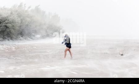 Donna che cammina attraverso una bianca con neve, vento forte e condizioni di neve al Great Sand Dunes National Park, Colorado Foto Stock