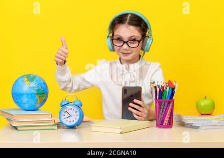 Ritorno a scuola e tempo felice. Carino bambino industrioso è seduto a una scrivania all'interno. Kid sta imparando in classe su sfondo giallo. Felice littl sorridente Foto Stock