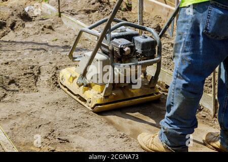 Il lavoratore usa il compattatore a piastra vibrante sotto costruzione a terra su nuova pavimentazione Foto Stock