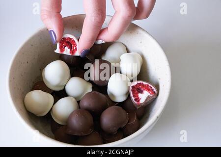 la mano della donna che sceglie e afferra fresco rosso e lucido fresco lamponi immersi in cioccolato bianco e nero fatto in casa Foto Stock