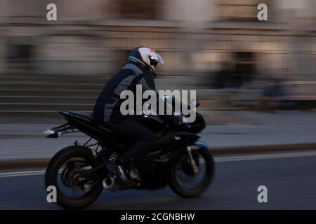 Primo piano immagine di un motociclista che guida una moto veloce da corsa su una strada nel centro della città. L'immagine viene acquisita a bassa velocità dell'otturatore per la sfocatura del movimento Foto Stock