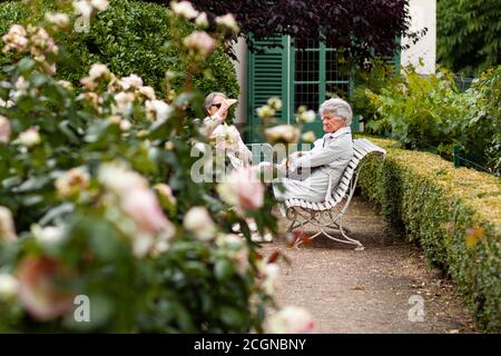 Parigi/Francia 06/13/2010: Tre donne anziane sono sedute su panchine decorative in un giardino di rose e stanno facendo una conversazione amichevole mentre si godono Foto Stock