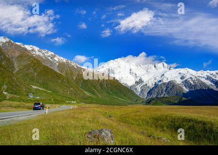 Le auto corrono sulle autostrade al mattino con cielo blu e nuvole in estate. Ci sono erba verde accanto alle strade nel Parco Nazionale del Monte Cook, Aoraki, Foto Stock