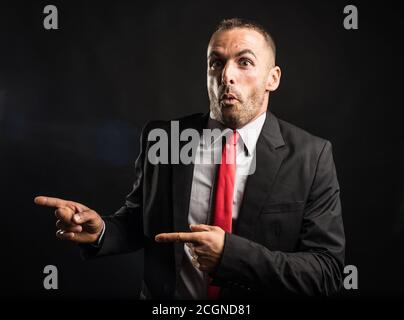 Uomo sorpreso in tuta che indica lo spazio di copia. Sfondo nero, scatto medio Foto Stock