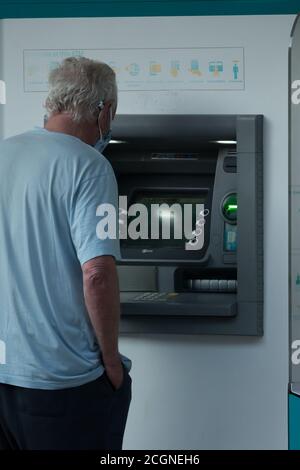 Uomo che indossa la maschera in piedi presso un ATM ritirando denaro a Città del Capo, Sud Africa Concept banking e tecnologia in Africa Foto Stock