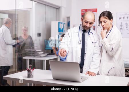 Lavoro di squadra di giovani medici in ospedale che indossano camici bianchi e stetoscopio guardando il computer portatile. Medica senior con pazienti anziani in età avanzata nel corridoio della clinica. Foto Stock