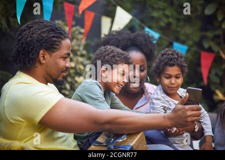 giovane padre afro-americano che mostra qualcosa alla sua famiglia su di lui telefono cellulare Foto Stock