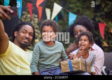 giovane padre afro-americano che prende selfie con la sua famiglia su di lui telefono cellulare Foto Stock