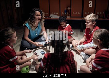 Allenatore femminile che si rilassa in un armadietto e si diverse a parlare per la squadra di calcio dei bambini Foto Stock