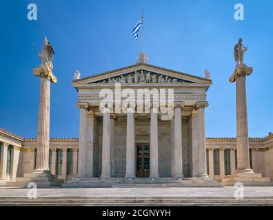 Ingresso principale dell'Accademia di Atene, centro di ricerca nazionale, colonne con Atena, antica dea greca, e Apollo, antico dio greco. Bandiera greca Foto Stock