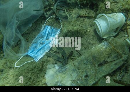 La maschera medica usata scartata si trova sul fondo marino insieme ad altri rifiuti di plastica, Becici, Budva regione, Montenegro Foto Stock