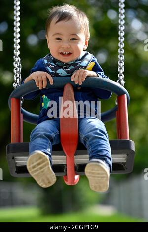 Bambino, ragazzo, 14 mesi, multietnico, su swing bambini, ride, Blaubeuren, Baden-Wuerttemberg, Germania Foto Stock