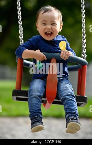 Bambino, ragazzo, 14 mesi, multietnico, su swing bambini, ride, Blaubeuren, Baden-Wuerttemberg, Germania Foto Stock