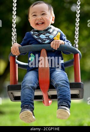 Bambino, ragazzo, 14 mesi, multietnico, su swing bambini, ride, Blaubeuren, Baden-Wuerttemberg, Germania Foto Stock