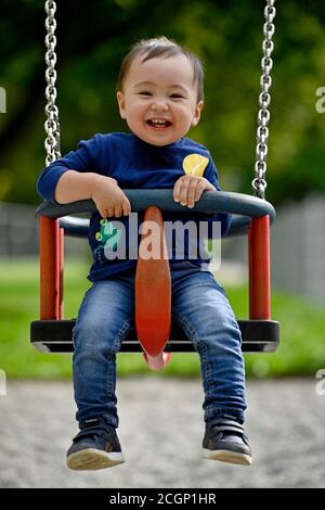 Bambino, ragazzo, 14 mesi, multietnico, su swing bambini, ride, Blaubeuren, Baden-Wuerttemberg, Germania Foto Stock