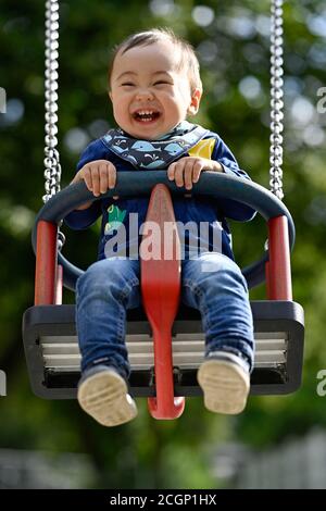 Bambino, ragazzo, 14 mesi, multietnico, su swing bambini, ride, Blaubeuren, Baden-Wuerttemberg, Germania Foto Stock