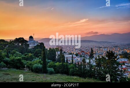 Vista di Atene, Grecia e le zone residenziali dalla collina di Pnyx in luce solare soffusa e il grande cielo del tramonto. Osservatorio nazionale di Atene in primo piano. Foto Stock