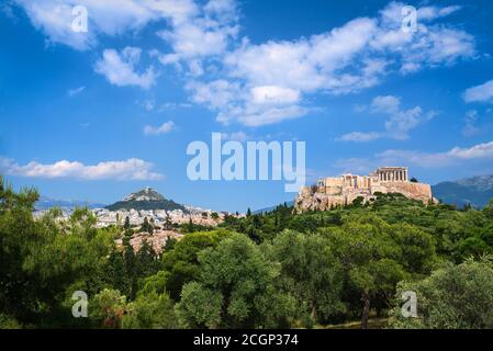 Vista iconica della collina dell'Acropoli e della collina di Lycabettus sullo sfondo di Atene, Grecia dalla collina di Pnyx nella luce del giorno d'estate con grandi nuvole nel cielo blu. Foto Stock