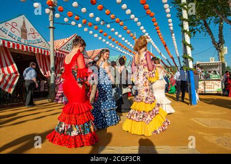 Donne in abiti colorati flamenco, di fronte a marchee, casetas, strada decorata, Feria de Abril, Siviglia, Andalusia, Spagna Foto Stock