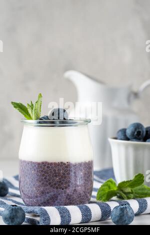 Sana colazione vegana di parfait al mirtillo a base di frutti di bosco freschi, yogurt al cocco, budino di chia e menta in un bicchiere su tovagliolo su tavola bianca Foto Stock