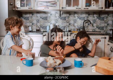 Una bella madre caucasica e due figli sono cosparsi di crema di cioccolato sul viso. Divertimento con i bambini Foto Stock