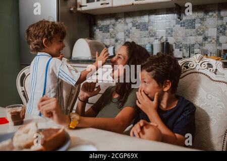 Una bella madre caucasica e due figli sono cosparsi di crema di cioccolato sul viso. Divertimento con i bambini Foto Stock