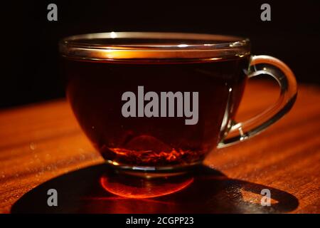 Tazza di vetro con tè nero sul tavolo di legno marrone. Primo piano, vista laterale in giornata di sole. Foto Stock