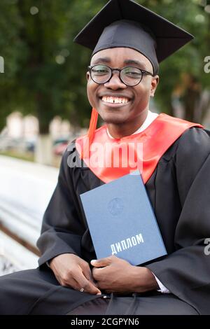 Bielorussia, la città di Gomil, 01 luglio 2020. Via della città. Afroamericano in un cappello di laurea con un diploma. Foto Stock