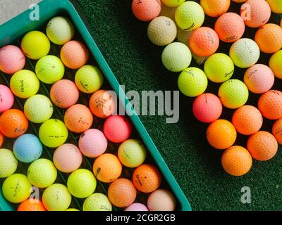 Palline da golf usate e colorate di marche assortite in un campo pratica. Foto Stock