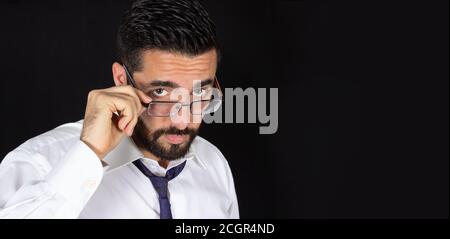 Ritratto di bel giovane bearded che guarda sopra gli occhiali in abbigliamento formale. Modello maschio ottico con spazio di copia. Attraente uomo d'affari di stile con ti Foto Stock