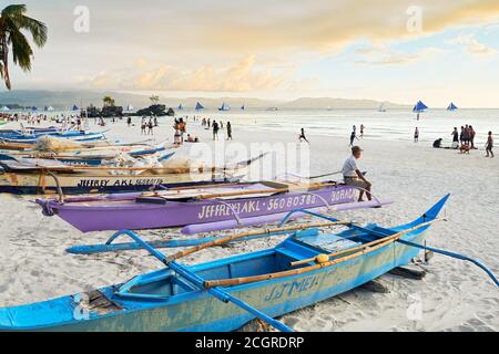 Un vecchio uomo seduto su una barca da pesca che guarda il tramonto e i turisti lungo la Spiaggia Bianca sull'Isola di Boracay, Visayas, Filippine, Asia Foto Stock