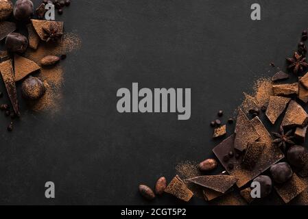 Cioccolato fondente. Pezzi di cioccolato, tartufi, cacao in polvere e spezie sul tavolo nero, vista dall'alto, spazio per la copia. Foto Stock