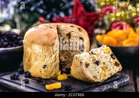 Fetta di delizioso panettone con frutta candita con luci di Natale offuscate e lampeggianti, pane con frutta Foto Stock