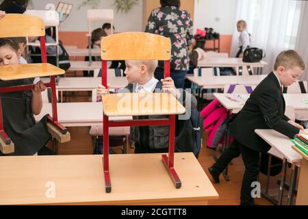 I first-graders hanno messo le sedie sulla scrivania alla fine delle lezioni alla scuola primaria rurale. Foto Stock