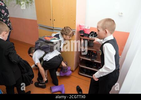 I primi classificati con gli zaini cambiano le scarpe davanti a un supporto in un angolo di classe dopo le lezioni nella scuola primaria rurale comunale. Foto Stock